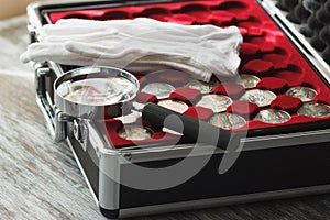 Different collector`s coins in the box with a magnifying glass and white gloves