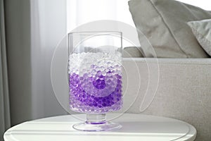 Different color fillers in glass vase on white table at home. Water beads