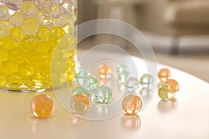 Different color fillers and glass vase on white table in room, closeup. Water beads