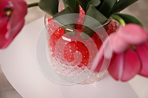 Different color fillers and tulips in glass vase, closeup. Water beads
