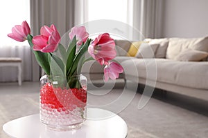 Different color fillers and tulips in glass vase on white table at home, space for text. Water beads