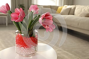 Different color fillers and tulips in glass vase on white table at home, space for text. Water beads