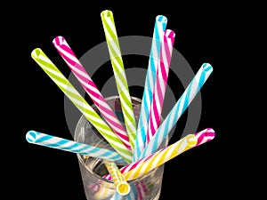 Different colored plastic drinking straws placed in a glass black background