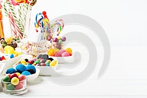 Different colorful candy sweets. Mix candy confectionery in jars on white wooden background with copy space