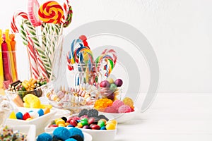 Different colorful candy sweets. Mix candy confectionery in jars on white wooden background with copy space