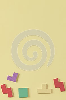 Different colorful shapes wooden puzzle blocks on yellow background. Geometric shapes in different colors, top view