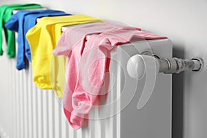 Different colorful socks hanging on white radiator indoors, closeup