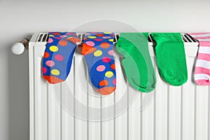 Different colorful socks on heating radiator near white wall