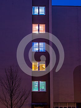 Different colors of lights in the windows of the building in the early evening