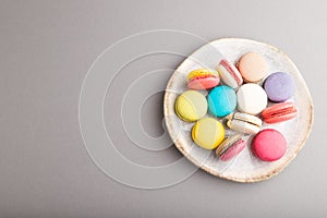 Different colors macaroons on ceramic plate on gray pastel background. side view, copy space