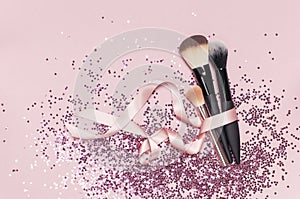 Different Cosmetic makeup brushes with pink ribbon and holographic glitter confetti in the form of stars on pink background Flat