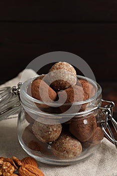 Different delicious vegan candy balls in glass jar and nuts on table