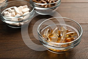 Different dietary supplements in glass bowls on wooden table, closeup