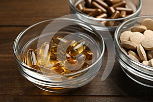 Different dietary supplements in glass bowls on wooden table, closeup