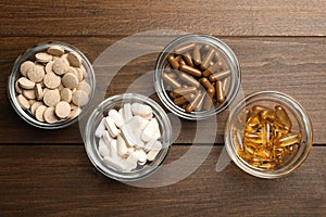 Different dietary supplements in glass bowls on wooden table, flat lay