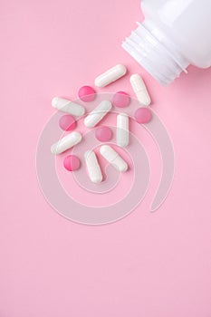 Different drugs falling from the white  bottle on pink paper background. Concept of pharmacy.