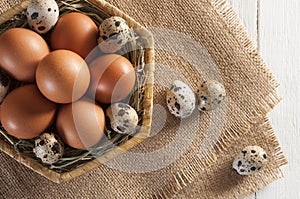 Different eggs in basker and on burlap. White wooden background.