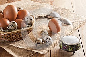 Different eggs in basket and on burlap. Near teaspoons and salt.