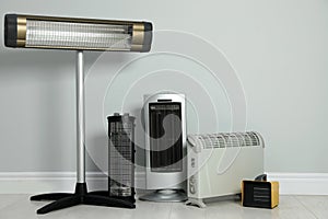 Different electric heaters near light grey wall indoors. Space for text photo