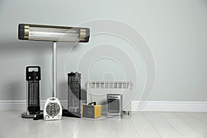 Different electric heaters near light grey wall indoors. Space for text