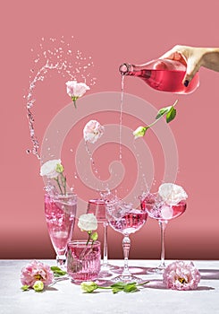 Different elegant champagne glasses with sparkling wine, women hand is pouring rose wine from bottle to coupe glass