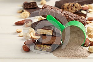 Different energy bars, nuts and protein powder on white wooden table, closeup