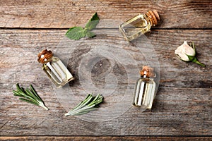Different essential oils in glass bottles and ingredients on wooden background
