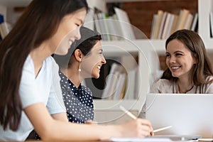 Different ethnicity students girls sitting at desk studying together