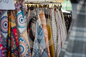 Different fabric and colors of scarf hanging on an open market. Garments such as scarves being sold on a market, multitude of them
