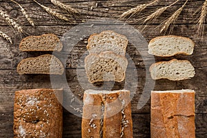 Different fresh bread and spikelets of wheat on rustic wooden background. Creative layout made of bread.