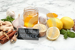 Different fresh products and card with phrase Natural Antibiotic on white marble table