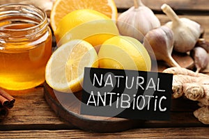 Different fresh products and card with phrase Natural Antibiotic on wooden table, closeup