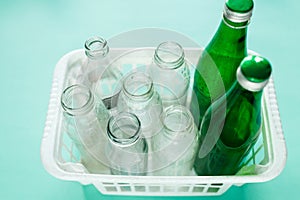 Different glass bottle wastes ready for recycling in white basket on green background. Social responsibility, ecology care,