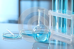 Different glassware and test tubes with light blue liquid on table in laboratory. Space for text