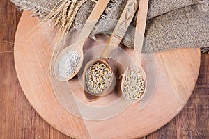 Different groats, whole barley grains in wooden spoons, top view photo