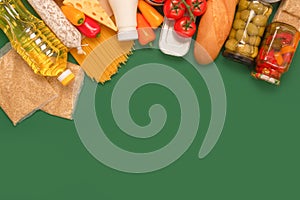 Different groceries, food donations on green background with copy space - pasta, vegatables, canned food, baguette