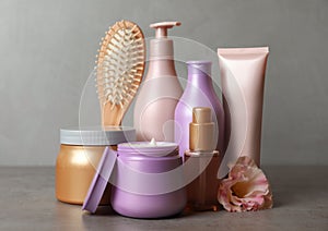 Different hair products, flower and brush on grey table