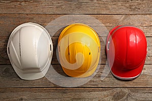Different hard hats on wooden background, top view.