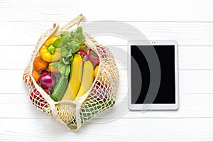 Different health food - yellow bell pepper, tomatoes, bananas, lettuce, green, cucumber, onions in mesh bag tablet with black touc