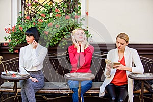 Different interests. Group pretty women cafe terrace entertain themselves with reading speaking and listening