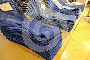 Different jeans folded on the wooden shelf in the store close-up. Casual style. Fashion retail denim business