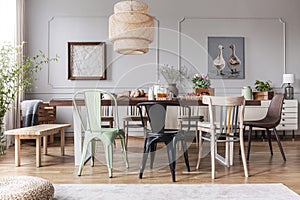 Different kid of chairs at table with flowers and food in rustic dining room interior with lamp and posters. Real photo