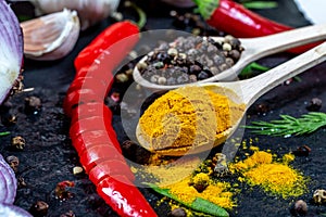 Different kind of spices and herbs, chili, garlic and onion on a black stone background