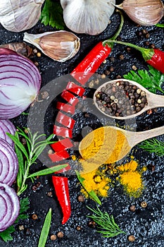 Different kind of spices and herbs, chili, garlic and onion on a black stone background. The view from the top. Flatley