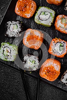 Different kind of sushi roll on on black plate on black concrete