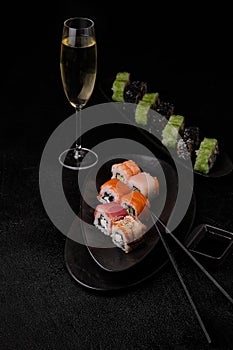 Different kind of sushi roll; chopsticks and glass of shampagne on black background