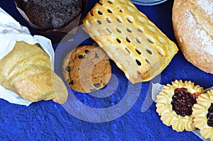 Different kinds of bread rolls on black board from above. Kitchen or bakery poster design. muffin, croissant, cookies