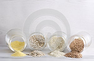 Different kinds of cereal in the glass jar.Heaps of cereals on the whiye kitchen table against bright wall, empty space for text