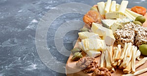 Different kinds of cheeses, dried apricots, whole-grain breads, nuts, olives, capers on a wooden board.
