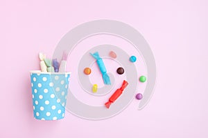 Different kinds of colorful candy out of a blue paper cup with white dot on pink background